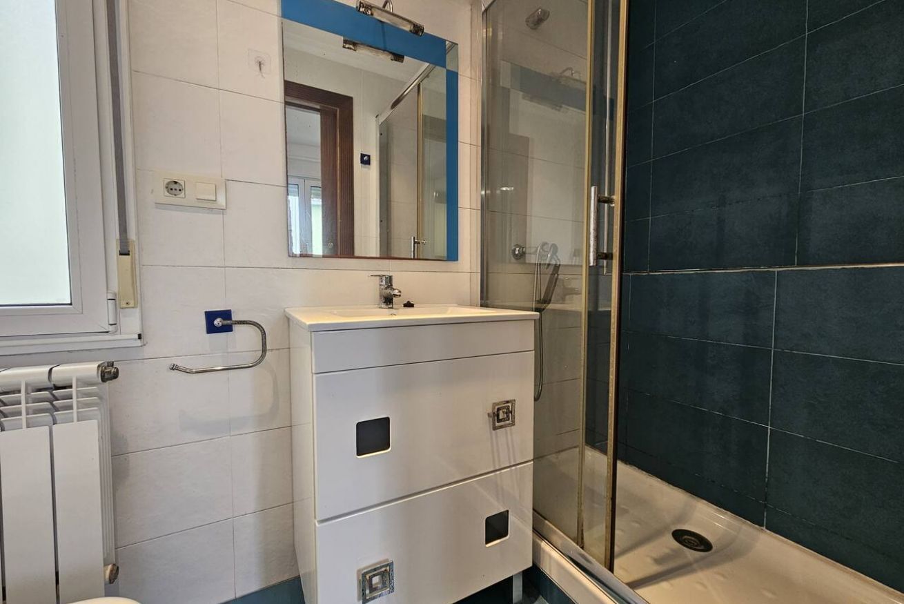 A bathroom with a white sink, a mirror, a glass shower enclosure, and a radiator.