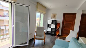 A living room with a sofa, a chair, a table, a bookshelf, and a sliding door to a balcony. - 10a05 Apartamento 2 dormitorios vistas al parque (Pravia)