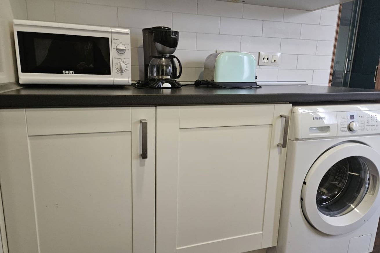 Eine Küche mit Mikrowelle, Kaffeemaschine, Toaster und Waschmaschine.