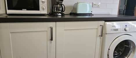 A kitchen with a microwave, coffee maker, toaster, and washing machine.