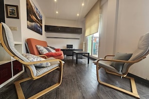 Una sala de estar moderna con dos mecedoras, un sofá, una mesa de centro y un televisor.