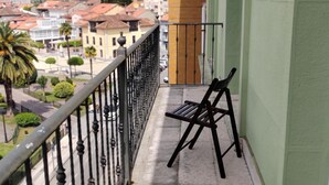 Ein Balkon mit Metallgeländer, einer Sitzbank und Blick auf eine Stadt mit Gebäuden und Bäumen.