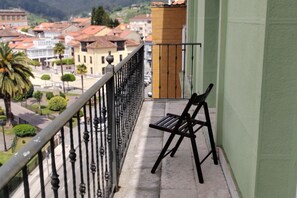 A balcony with a metal railing, a bench, and a view of a town with buildings and trees. - 10a05 Apartamento 2 dormitorios vistas al parque (Pravia)