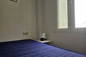 A room with a bed, a bedside table with a lamp, a window, and a wall socket. - 10a05 Apartamento 2 dormitorios vistas al parque (Pravia)