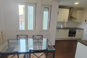 A compact kitchen with white cabinets, a built-in oven, and a dining area with a glass table and chairs.