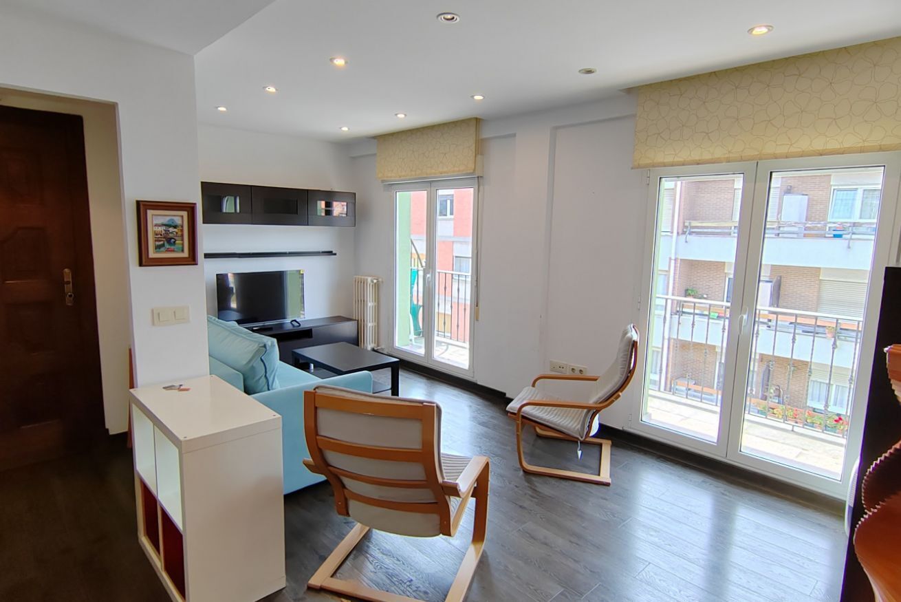 A modern living room with a sofa, two chairs, a TV, and a kitchen area.