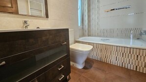 A bathroom with a dark vanity, a white toilet, a bathtub, and a patterned wall. - 10a05 Apartamento 2 dormitorios vistas al parque (Pravia)