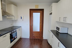 A kitchen with white cabinets, a microwave, a stove, and a wooden door. - 10a05 Apartamento 2 dormitorios vistas al parque (Pravia)