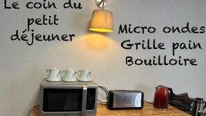 Une petite cuisine équipée d’un four à micro-ondes, d’un grille-pain et d’une bouilloire, le tout posé sur un plan de travail en bois. On peut y voir trois théières blanches, placées sur le dessus du four à micro-ondes.