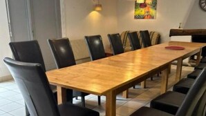 Un espace repas avec une longue table en bois, des chaises noires, des luminaires suspendus et un tableau au mur.
