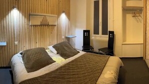 Une chambre d’hôtel avec un lit, un bureau, une chaise, un radiateur et un tableau au mur.