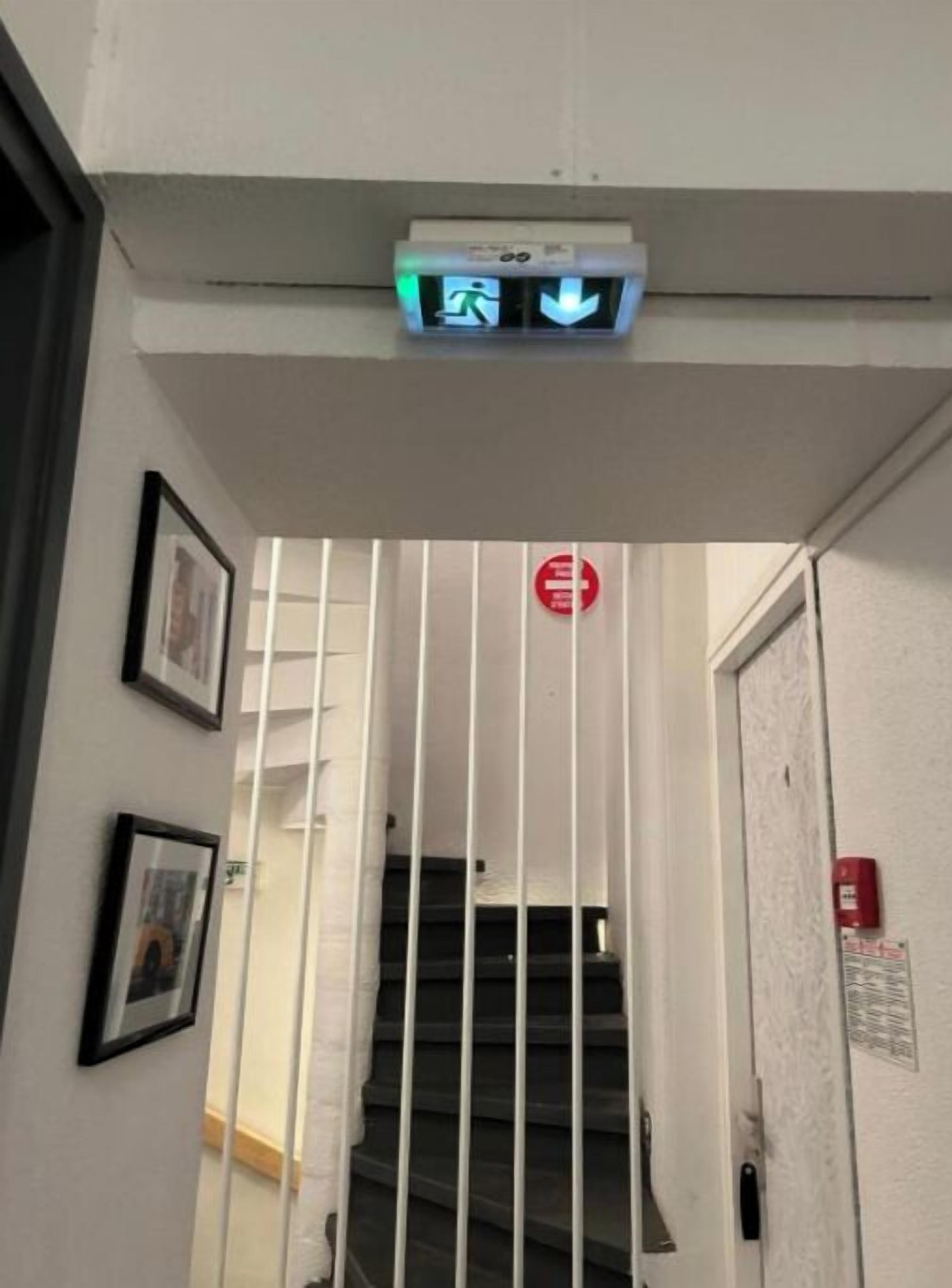 Un escalier avec un panneau rouge indiquant « accès interdit », une alarme incendie et une barrière de sécurité.