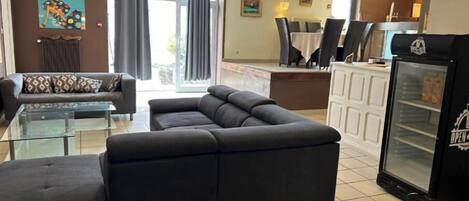 A modern living room with a sectional sofa, a glass coffee table, and a dining area with a table and chairs.