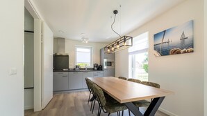A modern kitchen with a dining area, featuring a wooden table and chairs, a hanging light fixture, and a painting on the wall. - Holiday Home by Lake Beach Simonshaven (Simonshaven)