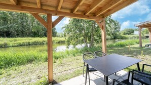 A wooden pavilion with a table and chairs overlooking a river and greenery. - Holiday Home by Lake Beach Simonshaven (Simonshaven)