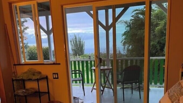 Ein Schlafzimmer mit einem großen Bett, einem Sessel, einem kleinen Tisch und einer Schiebetür zu einem Außenbereich mit Blick auf Himmel und Bäume.
