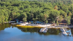 A lakeside resort with boats docked, a sandy beach, and a forested area.