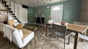 Een kamer met een visgraatvloer, een bank, een eettafel met stoelen, een open haard en een trap.