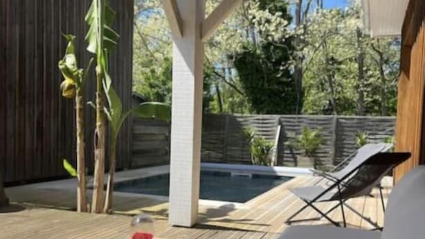 A covered patio with a wooden table, a white sofa, and a pool in the background. - Villa with pool near the lake (CAZAUX)