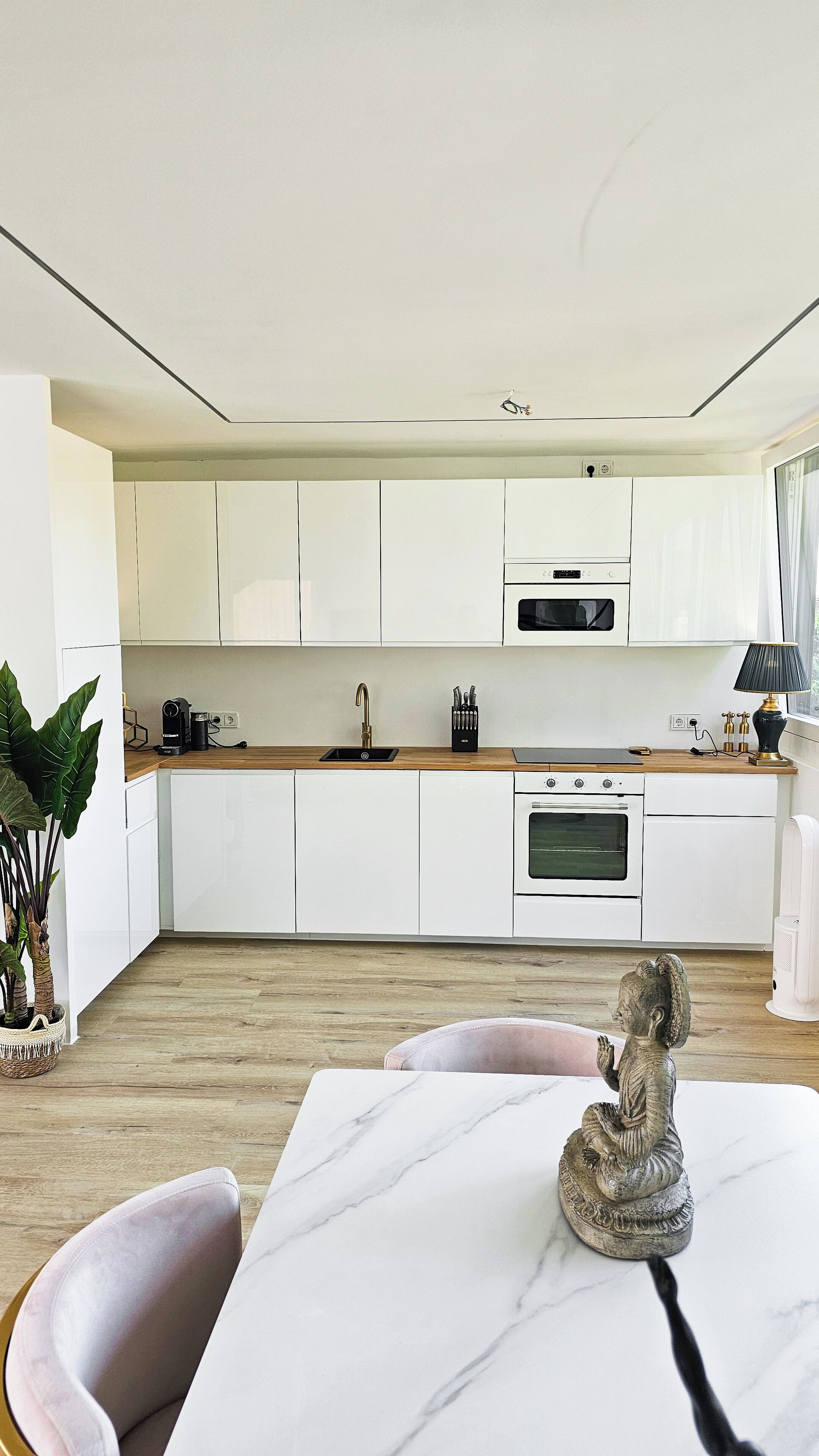 A modern kitchen with white cabinets, a marble countertop, and a dining area with a table and chairs.