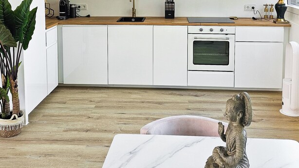Una cocina moderna con armarios blancos, encimera de mármol y comedor con mesa y sillas.