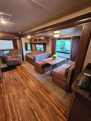Cozy seating area with a cushioned bench and chair, wooden cabinets, and a kitchen area.