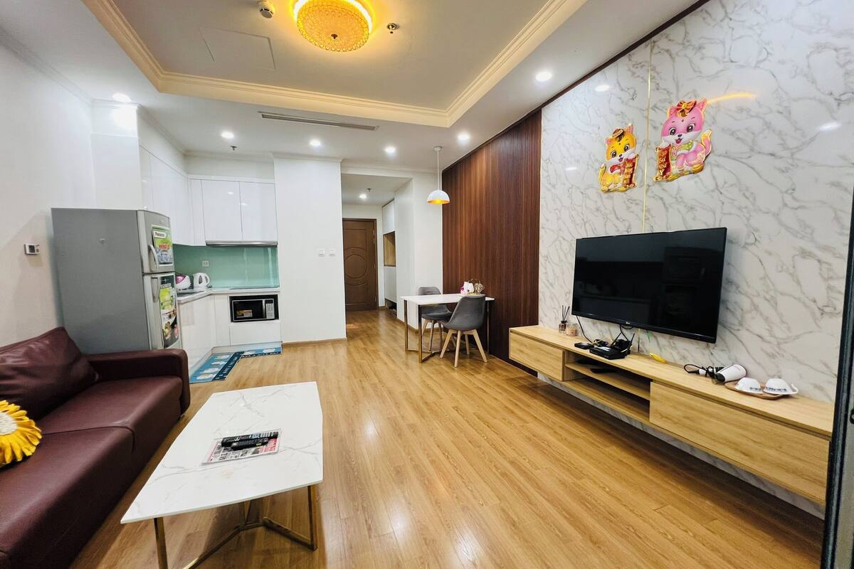 Un salon moderne avec un canapé, une table basse, un téléviseur et un coin cuisine à l’arrière-plan.