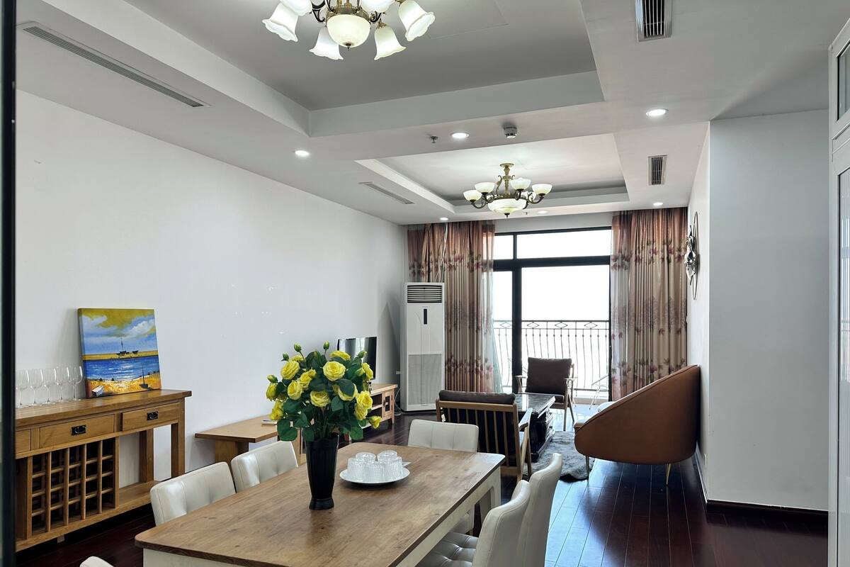 Un espace repas moderne avec une table en bois, des chaises blanches, un vase de fleurs jaunes et un tableau accroché au mur.