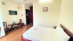 Habitación de hotel con una cama, un escritorio con silla, televisor y una puerta.