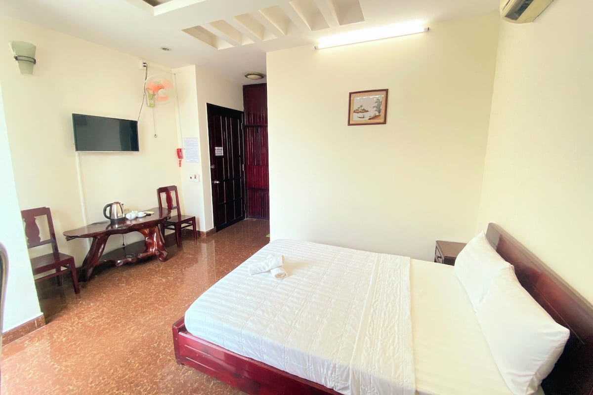 A hotel room with a bed, a desk with a chair, a television, and a door.