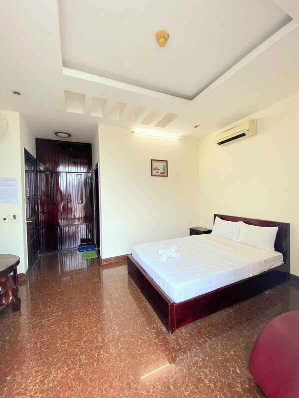 Habitación de hotel con una cama grande, una lámpara de techo, un equipo de aire acondicionado y una puerta de madera.