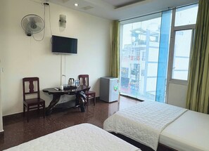 Habitación de hotel con dos camas, televisión, mesa con sillas, refrigerador y ventana con cortinas.