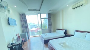 Habitación de hotel con dos camas, un escritorio con silla, un televisor y un ventanal con cortinas.