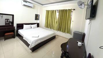 Quarto de hotel com cama, escrivaninha, cadeira, televisão e janela com cortinas.
