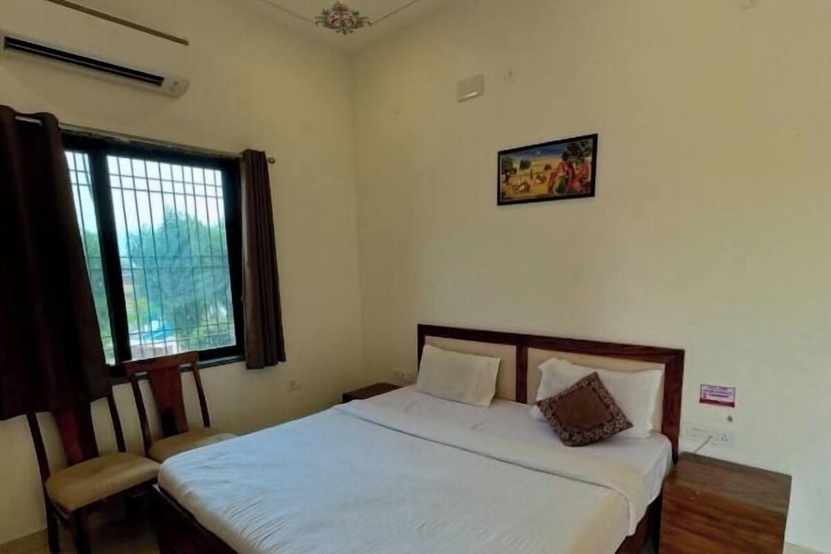 A bedroom with a large bed, a chair, a window with curtains, a painting on the wall, and a nightstand.