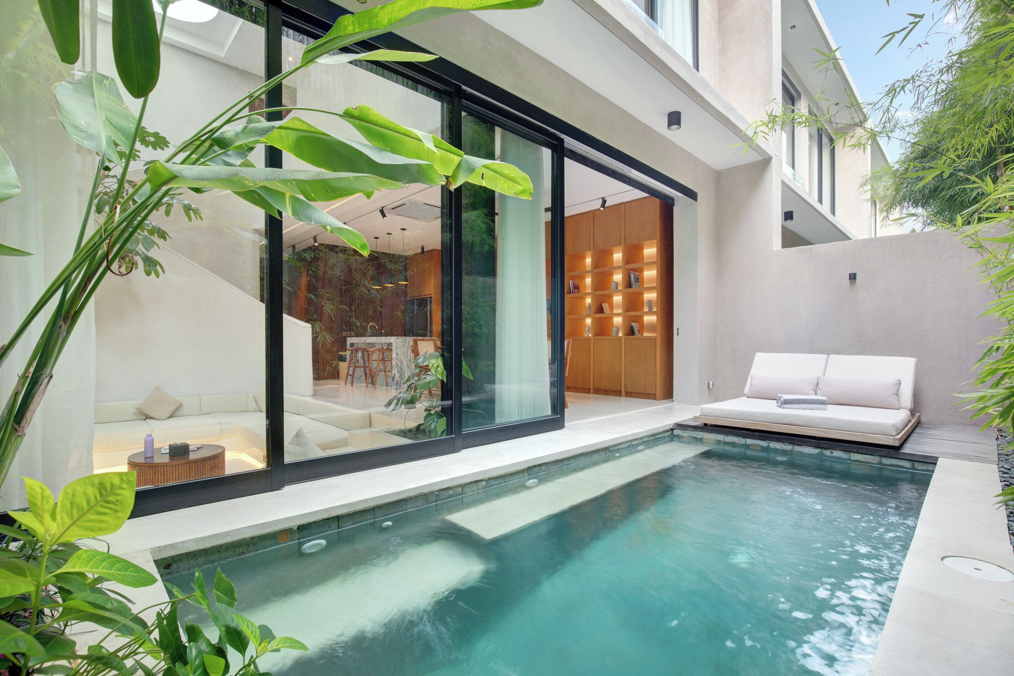 A modern outdoor pool area with a glass-enclosed seating area and a wooden bookshelf.