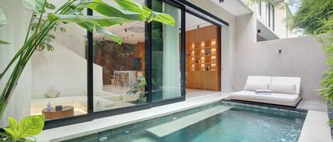 A modern outdoor pool area with a glass-enclosed seating area and a wooden bookshelf.