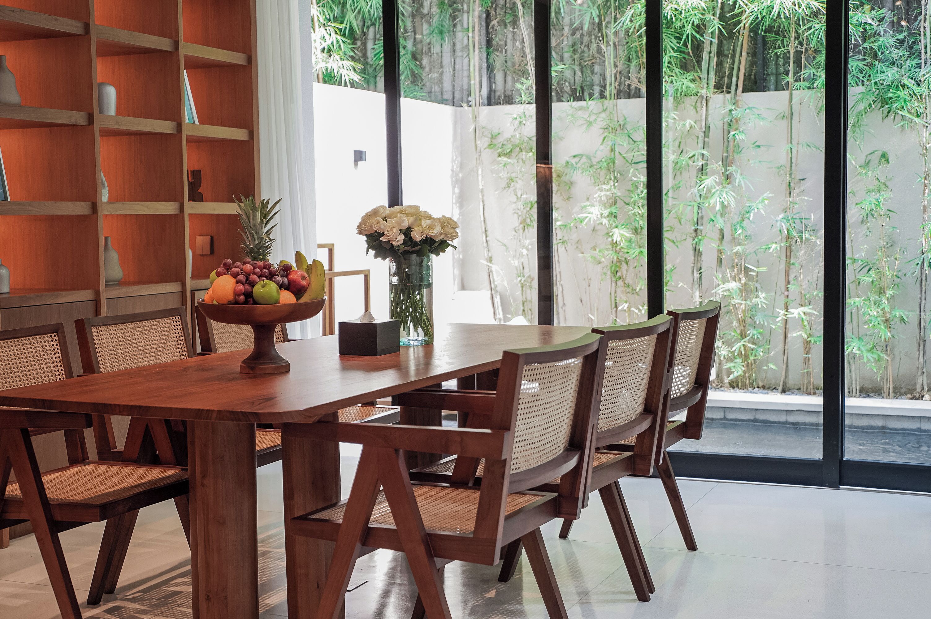 A dining area with a wooden table and chairs, a fruit bowl, and a vase of flowers.