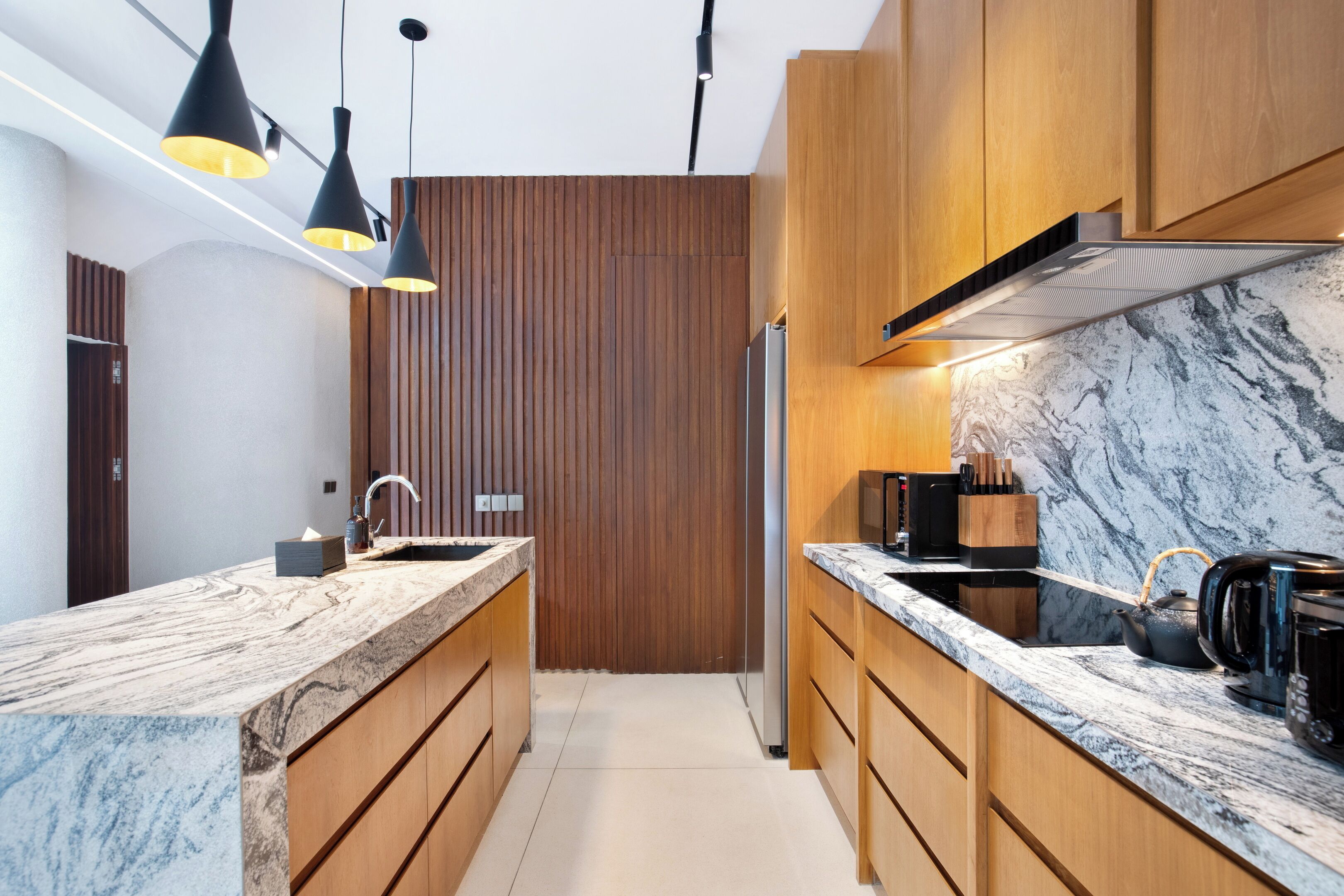 A modern kitchen with wooden cabinets, a marble countertop, and pendant lighting.