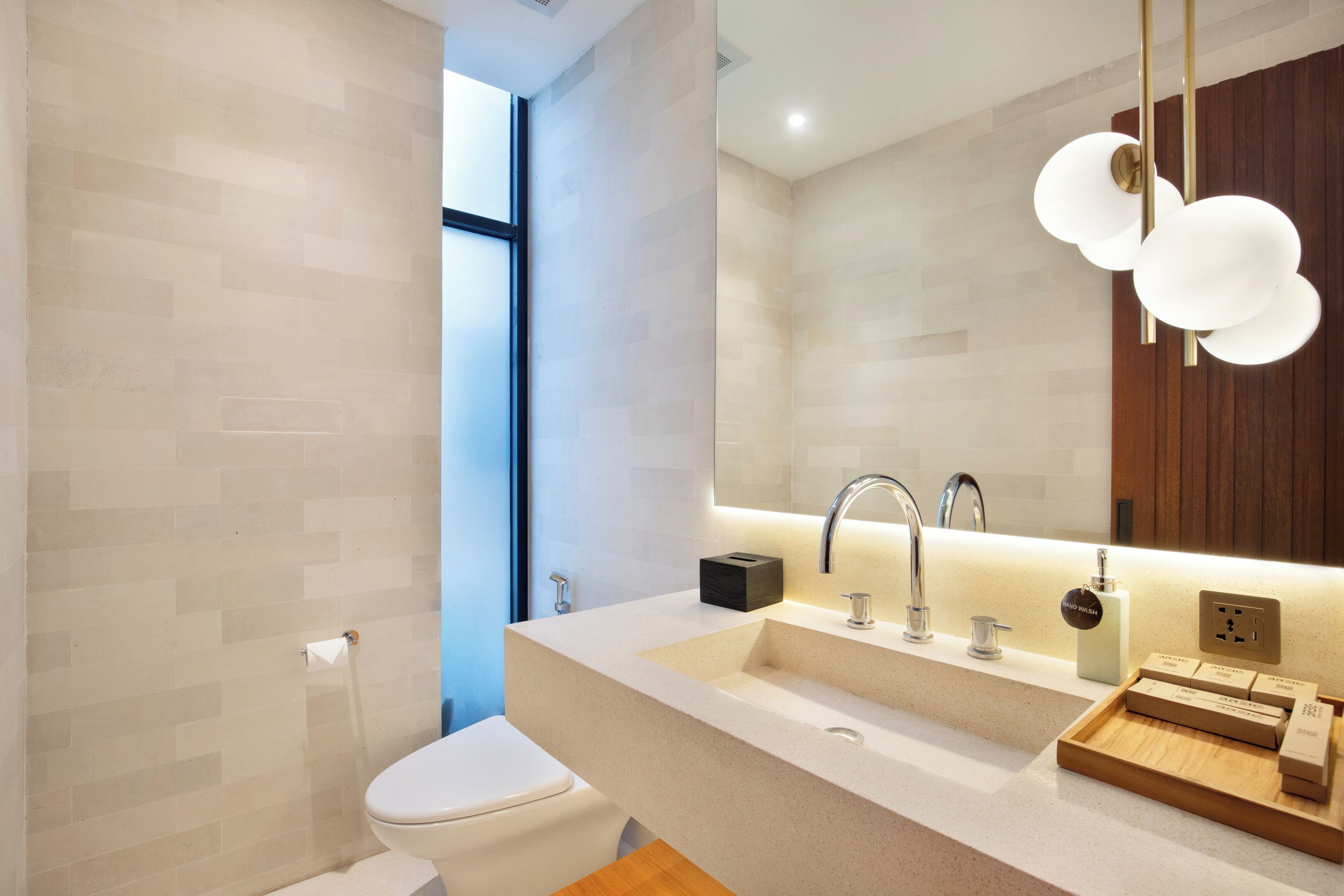 Une salle de bain moderne avec des toilettes blanches, un lavabo beige agrémenté d’un plateau en bois, et un grand miroir au-dessus du lavabo.