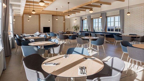 Un vaste espace dédié à la salle à manger, avec des tables rondes, des chaises bleues et des luminaires suspendus.