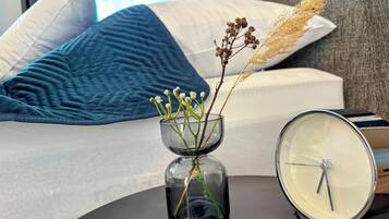 Ein Bett mit blauer Decke und Kissen, ein Nachttisch mit einer Glasvase voller Blumen und eine Uhr.