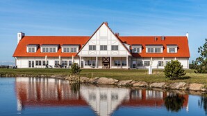 Un grand bâtiment blanc, surmonté d’un toit rouge, qui se reflète dans une étendue d’eau calme.