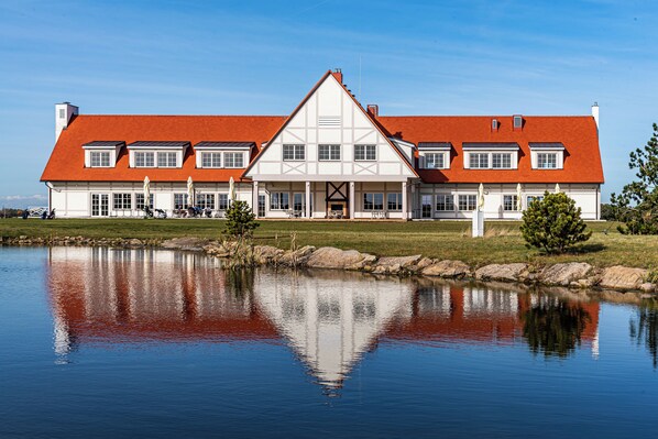 A large, white building with a red roof, reflecting in a calm body of water.