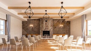 Une salle de conférence avec des chaises blanches disposées en rangées, un plafond en bois et un mur en pierre sur lequel est accrochée une télévision.