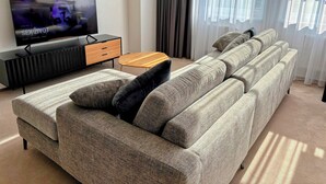 Un salon moderne avec un canapé d’angle gris, une table basse en bois et un téléviseur posé sur un meuble noir.