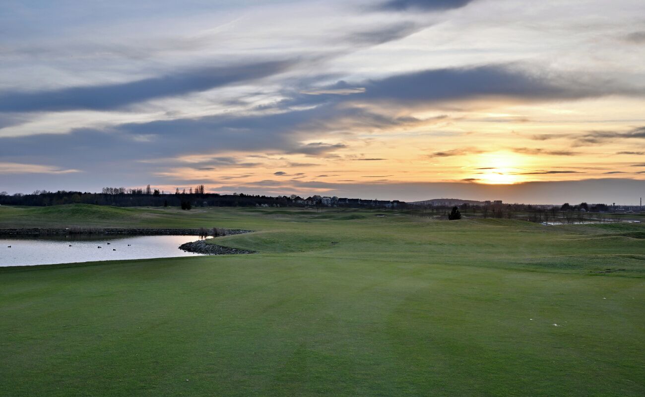 Ein Golfplatz mit Teich, Bäumen und Sonnenuntergang im Hintergrund.