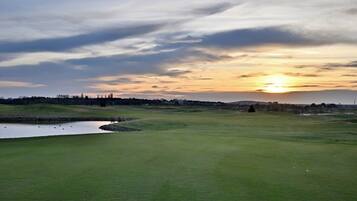 Ein Golfplatz mit Teich, Bäumen und Sonnenuntergang im Hintergrund.