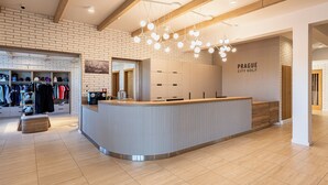 Un espace d’accueil moderne avec un comptoir en bois, un mur en briques et une enseigne indiquant « Prague City Golf ».