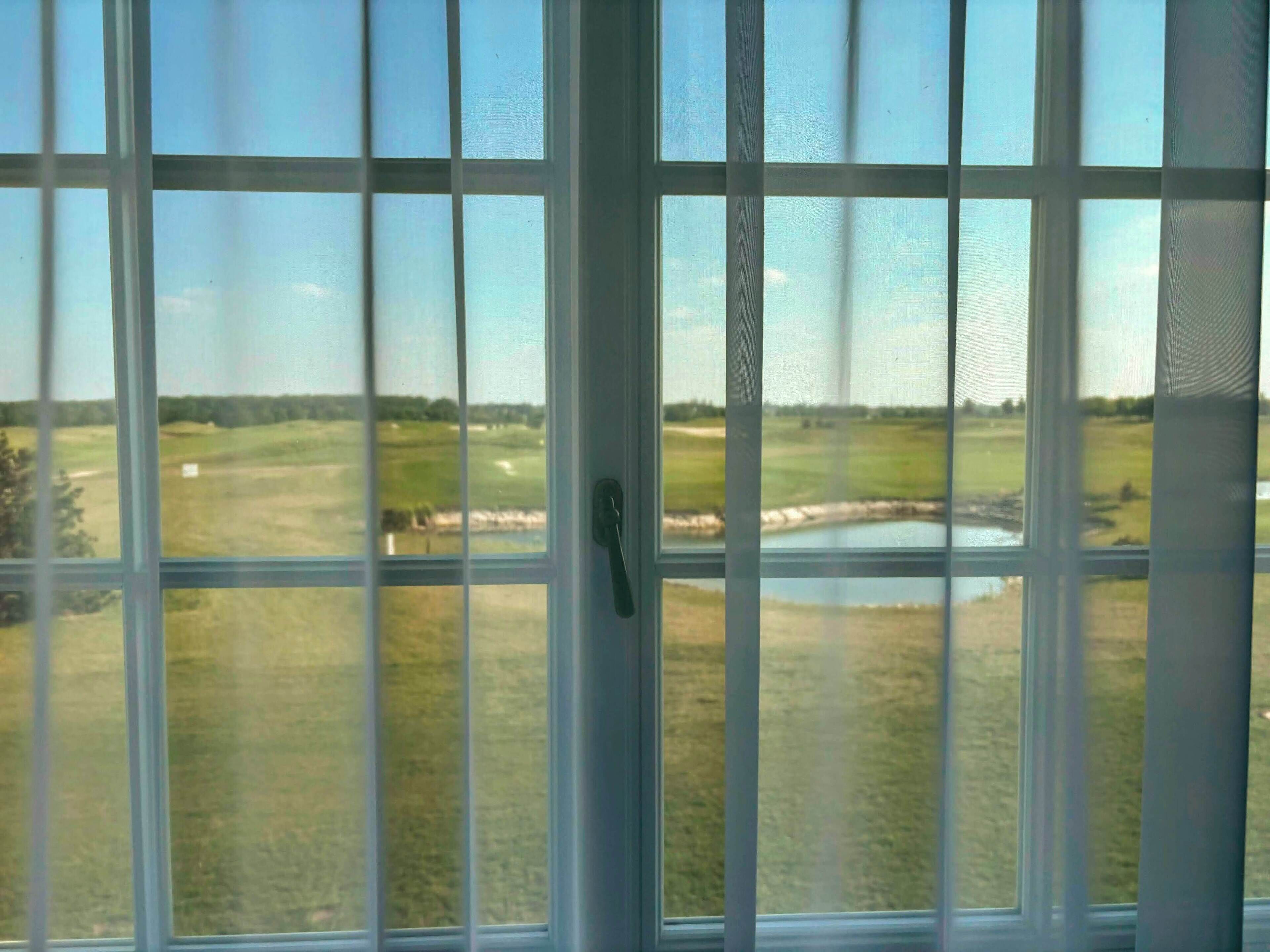 Une vue à travers une fenêtre donnant sur un terrain de golf et un étang.